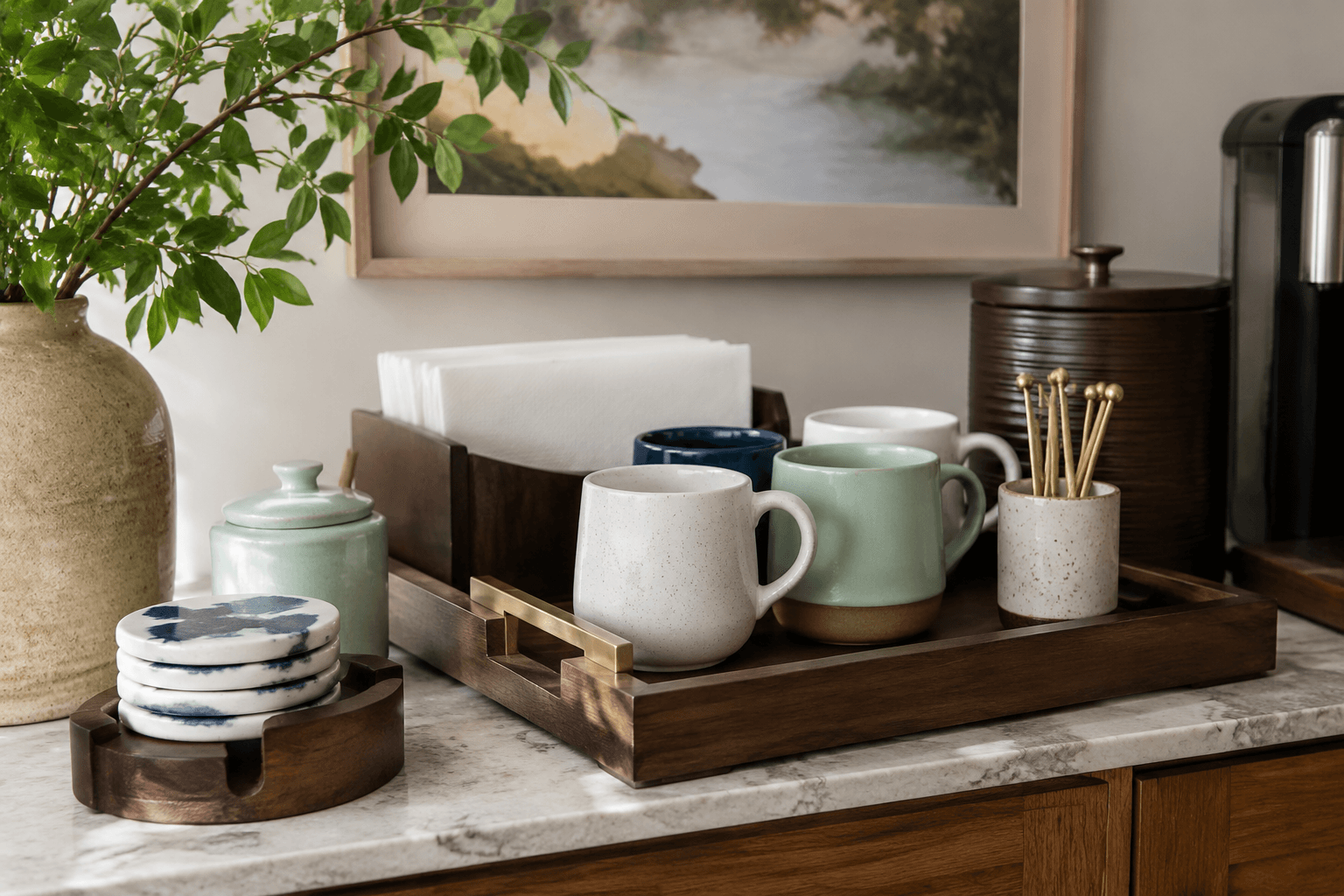 A styled home drink station with ceramic coasters, a tray, a stirrer cup and mugs